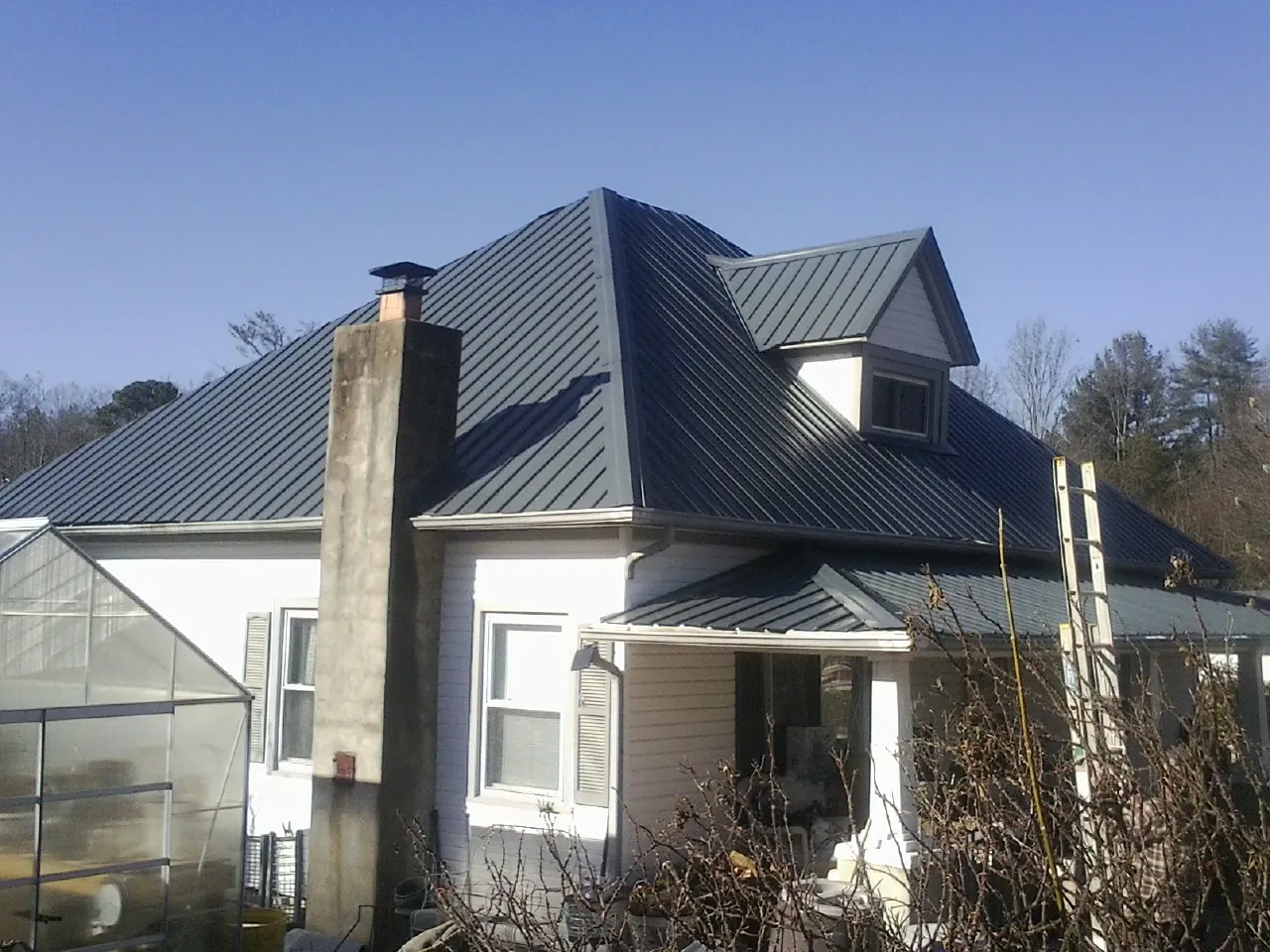 Dark blue standing seam metal roof on a white farmhouse with dormer — Slate & Tile Roof Repair by Roofing Brothers in Nelliston