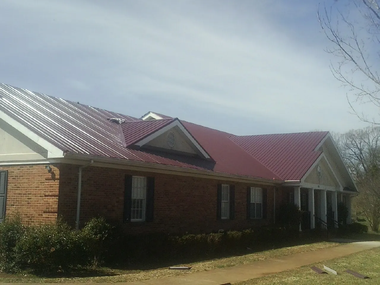 Red metal roof with gabled entries on a long brick building, from a Hail Damage Roof Repair job in Nelliston