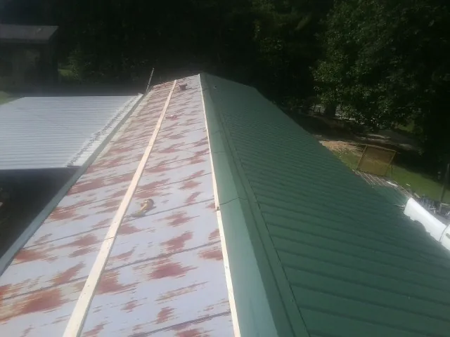 Old rusted panels beside newly installed green metal roofing — Wind Damage Roof Repair by Roofing Brothers in Nelliston