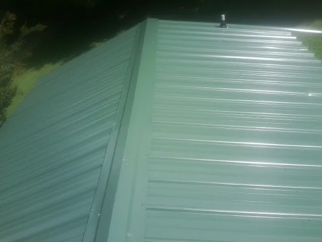 New green metal panels meeting at the ridge of a roof — Flat Roof Repair work by our crew in Nelliston