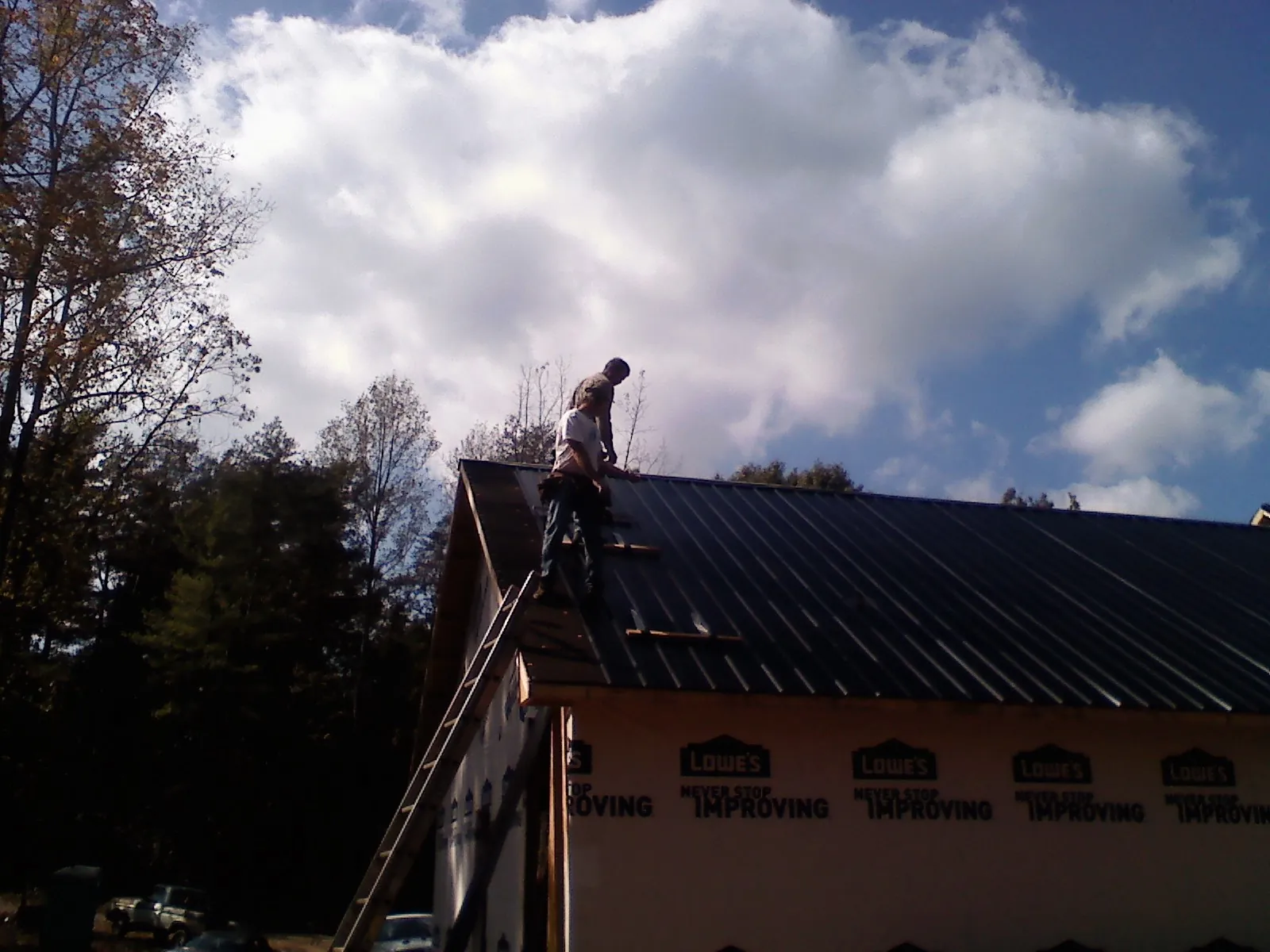Roofer fastening dark metal panels high against a cloudy sky, from a Roof Inspection job in Nelliston