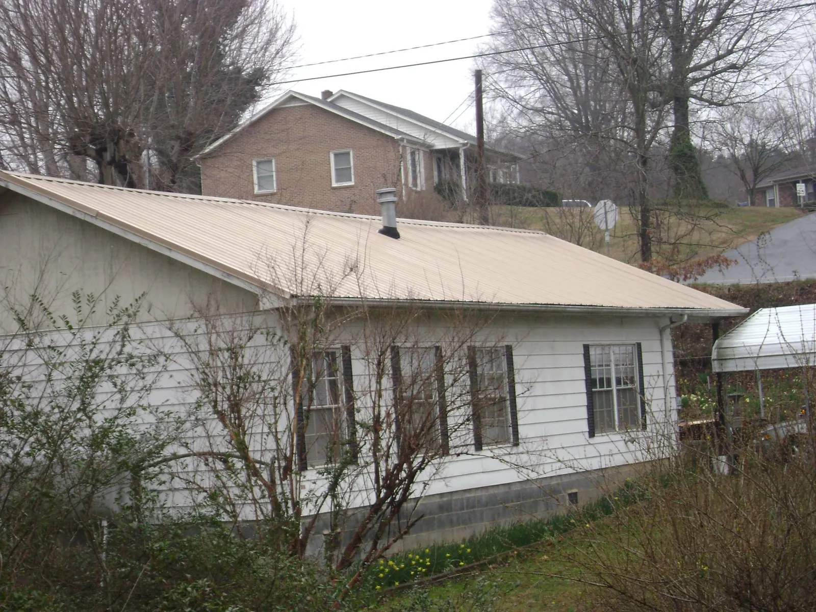 Tan metal roof on a white sided house set into a hillside — Commercial Roofing by Roofing Brothers in Nelliston